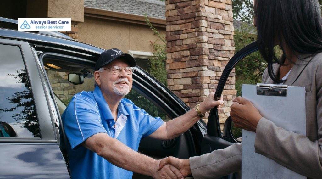 A smiling senior man wearing a U.S. Army cap shaking hands with a caregiver outside his home, symbolizing a warm welcome and personalized care.