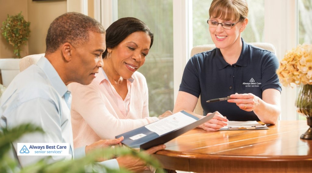 An Always Best Care senior services professional sitting at a table with a middle-aged couple, reviewing documents and discussing care options in a bright home setting.