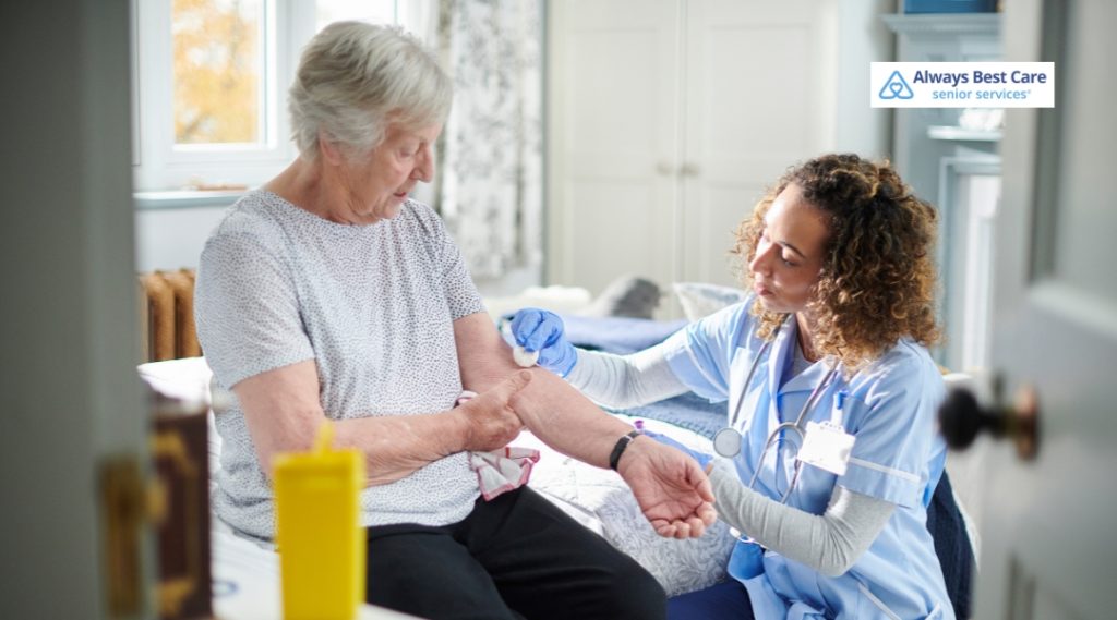 A nurse in blue scrubs administers an injection to an elderly woman at home, providing professional medical care.