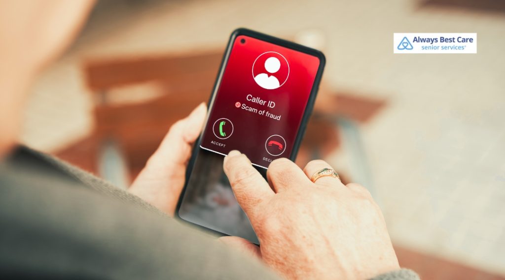 A close-up, over-the-shoulder view of an older person’s hands holding a smartphone. The phone screen shows an incoming call with a red background, a warning icon, and text reading "Caller ID: Scam of fraud." The person's finger is poised over the screen. An Always Best Care Senior Services logo is in the top right corner.