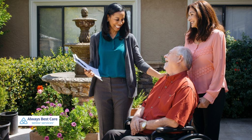 <strong>Unlocking Independence: Advocating for Wise Choices Among Kitchener’s Seniors</strong> 5 Posts A caregiver is assisting an elderly man in a wheelchair, smiling, while his family members are interacting with him. The Always Best Care logo is in the bottom left corner.