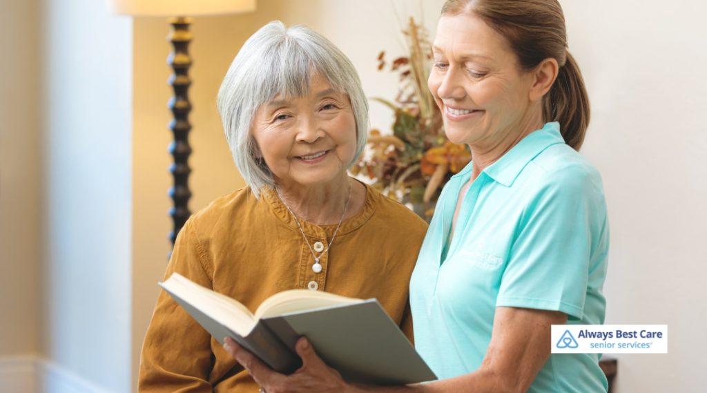A caregiver and senior enjoying a book together in a sunlit living room.