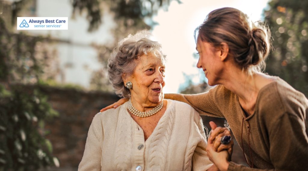 Senior woman smiling while holding hands with a caregiver outdoors, showcasing meaningful connection through companion care.